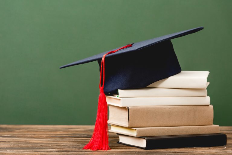 books and academic cap on wooden surface isolated on green