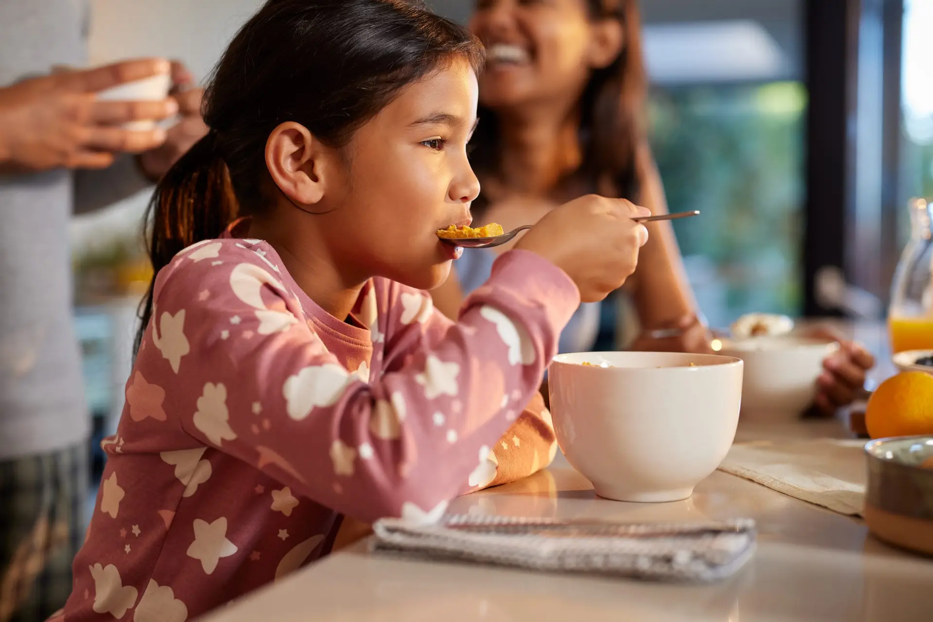 Indian cute little girl enjoy eating cereal for morning breakfast with appetite. Hungry female multiethnic kid holding full table spoon of sweet delicious corn oat flakes with milk. Healthy and nutrition meal in the morning.